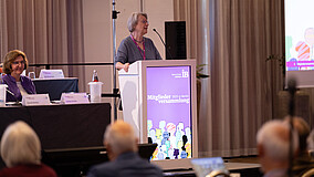 Frau spricht vor Publikum an einem Rednerpult.