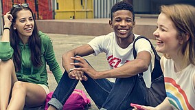 Mehrere Jugendliche sitzen zusammen und lachen, eine Person hält ein Handy in der Hand.