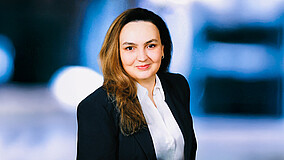 Jüngere Frau mit Blazer und längeren hellbraunen Haaren lächelt in die Kamera.