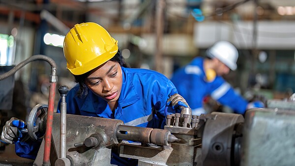 Frau mit Helm arbeitet an einer Maschine