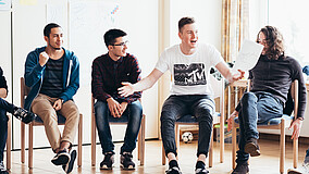 Junge Männer sitzen bei einem Workshop in einer Stuhlreihe.