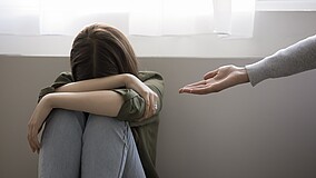 Mädchen hockt und hält sich die Hände vors Gesicht, während ihr eine Hand gereicht wird